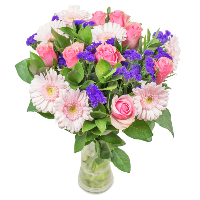 A lush and thoughtfully assembled floral bouquet, poised in a clear glass vase, draws in the eye with its harmonious blend of soft and mid-toned pinks. Around seven to nine roses, their petals partly furled in classic spirals and some still hugging tightly, anchor the centre-emblems of grace and affection. Clustered between are five to seven pale pink gerbera daisies, each displaying large, round blooms and slightly lighter centres, hallmark features of florist quality. Sprigs of vibrant purple statice are deftly threaded throughout the arrangement, delivering a striking burst of colour and texture. Verdant green foliage fans beneath, capturing the essence of Cranham's open spaces and revitalizing every view with its freshness. Through the clear glass vase, stems are visible in crisp, clear water, underscoring the bouquet's hand-tied immediacy and suitability as a just-arrived gift. This arrangement from Flowers Cranham, whether delivered for milestone birthdays, anniversaries, or simply to bring a touch of cheer to an Upminster Road office, is a visual poem of celebration and sincere sentiment-a fitting tribute to the joy Cranham brings its residents.